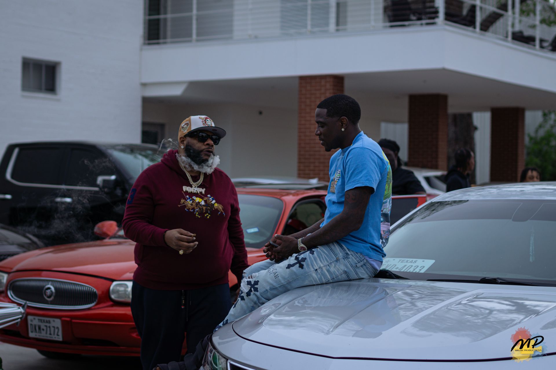 Two people talking beside parked cars outside a building