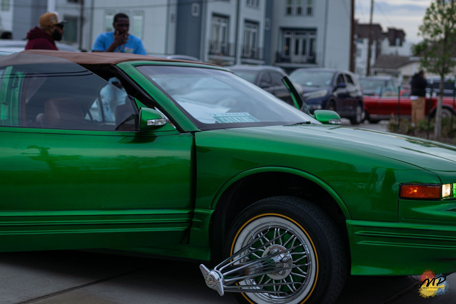 Green classic car with chrome wire wheels parked on a city street.