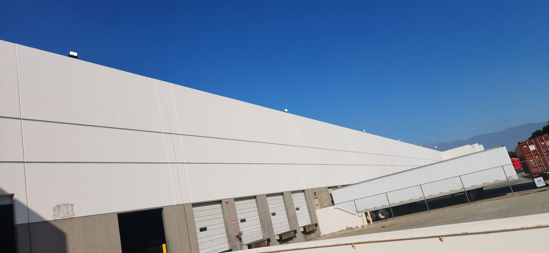 A white warehouse with several loading docks, a white trailer, and a blue sky.