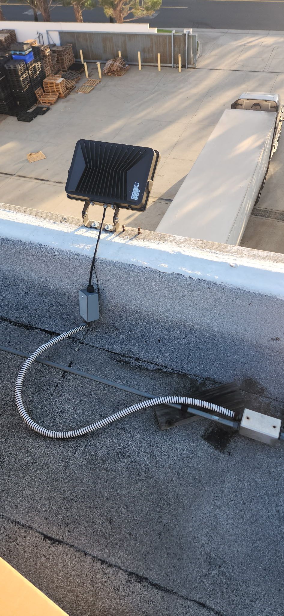 A black device with wiring on a rooftop, overlooking a concrete road and building materials.