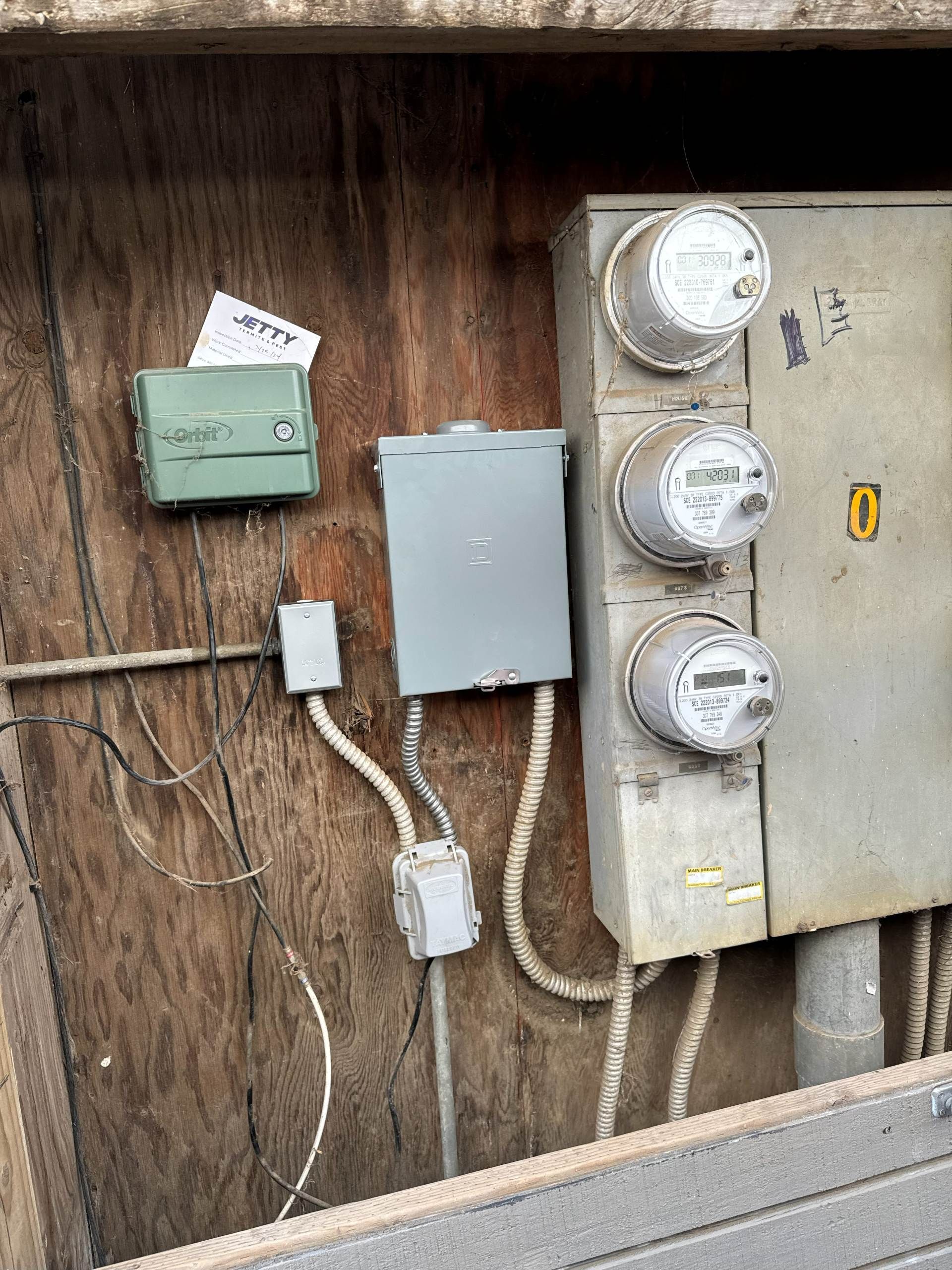 Outdoor electrical equipment, including meters, boxes, and wiring, mounted on a wooden surface.
