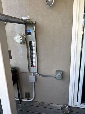 Exterior electrical panel on a stucco wall with a meter and conduit. Gray and white colors.