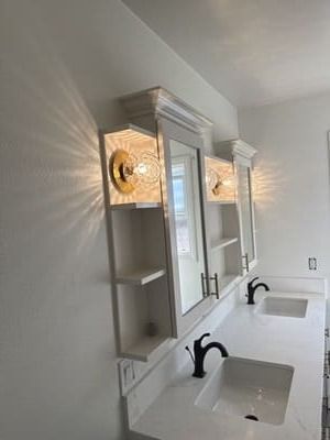 Bathroom with white cabinets, gold light fixtures, black faucets, and white countertop.