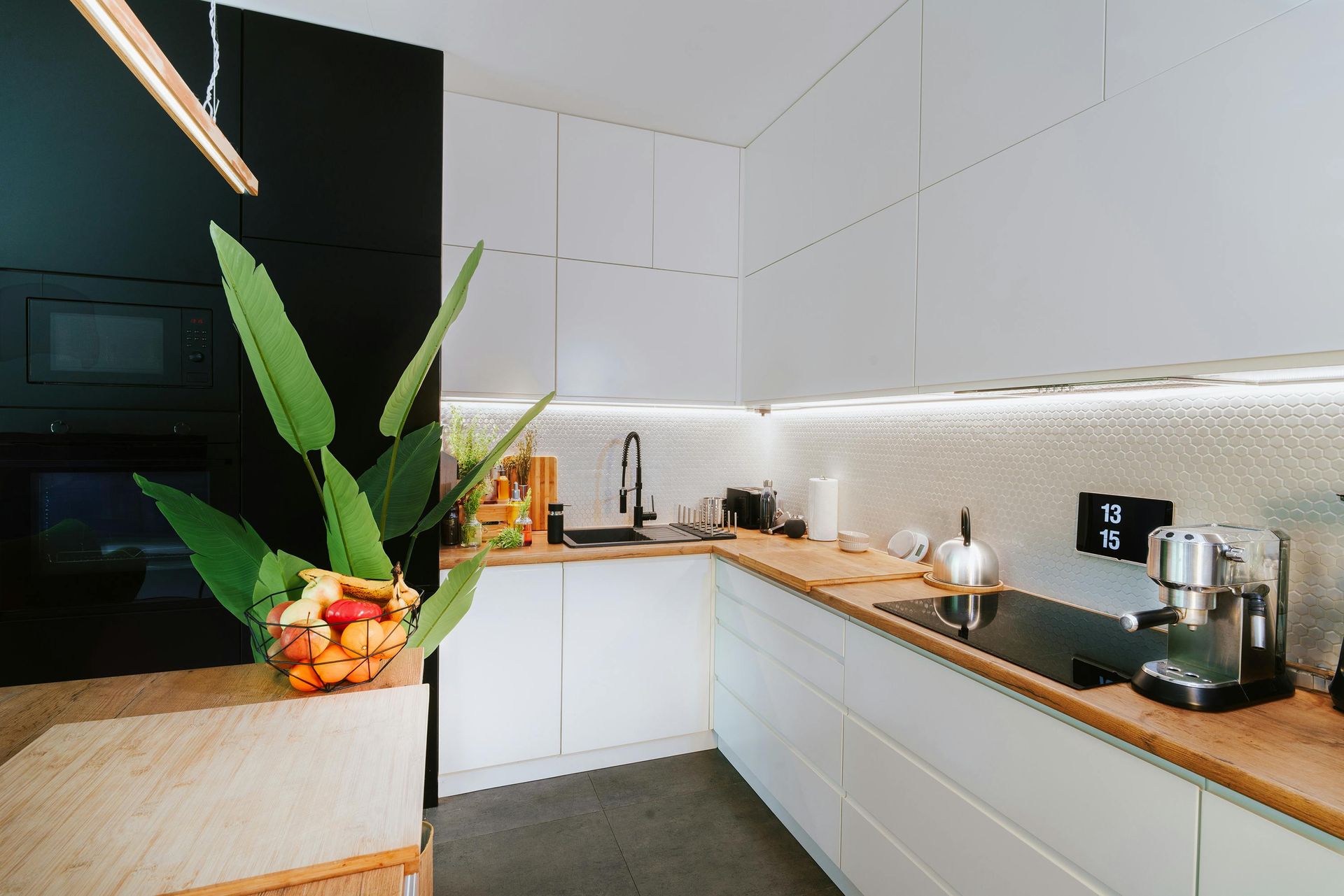 Modern white kitchen with wooden countertops, black appliances, and a plant.