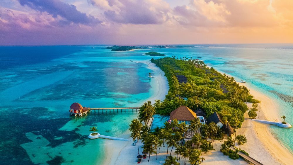Tropical island with overwater bungalows, turquoise water, and white sand beaches.