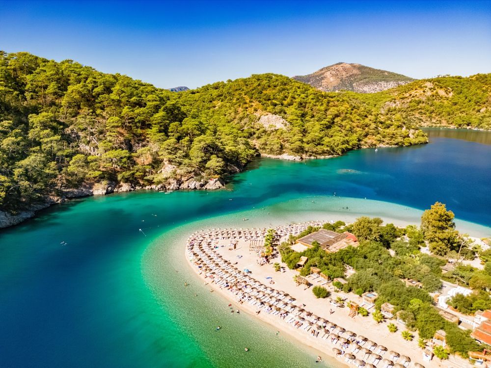 Aerial view of turquoise lagoon beach, surrounded by green trees and mountains.