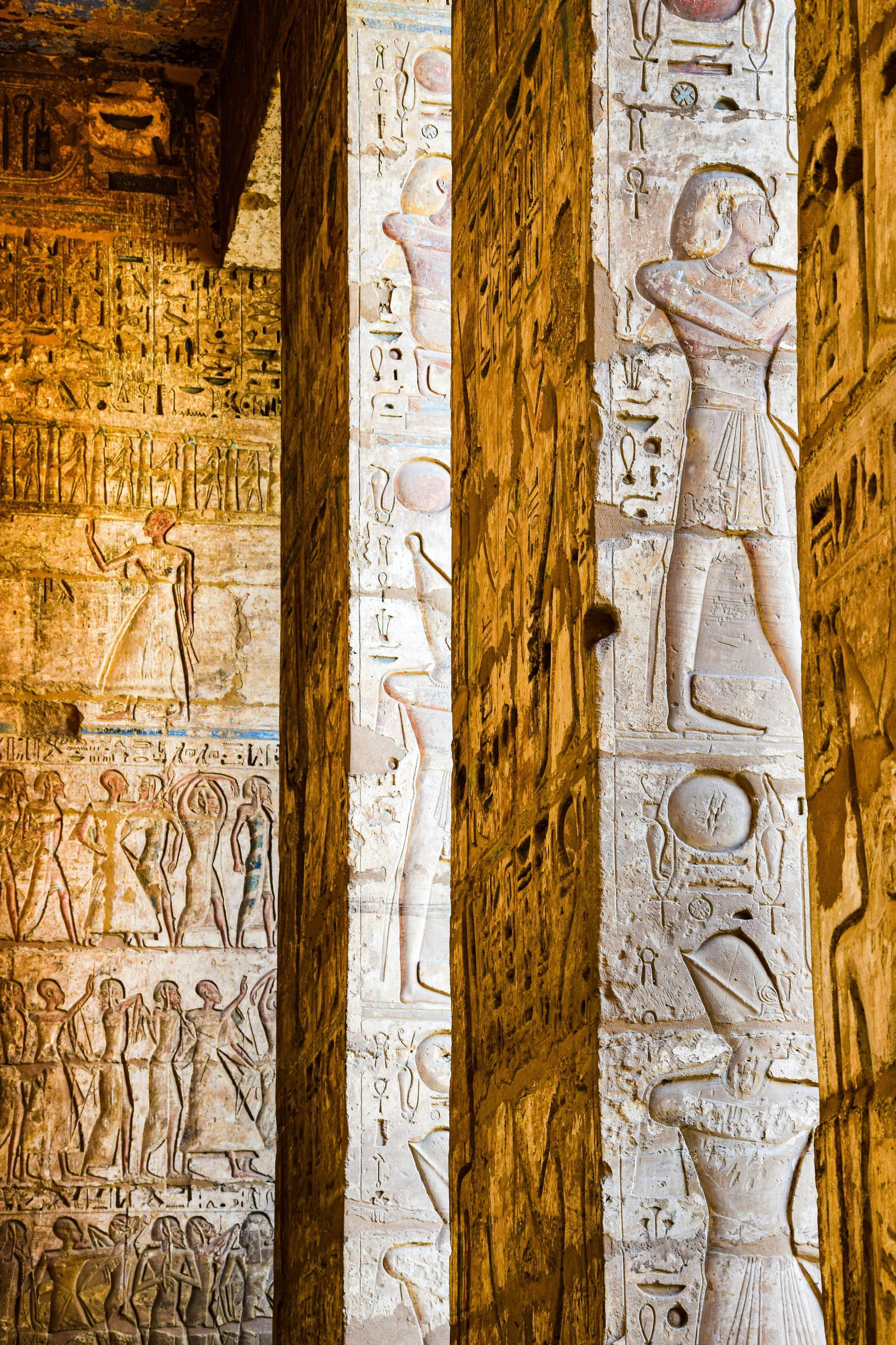 Stone columns with hieroglyphs and carved figures within an ancient Egyptian temple.