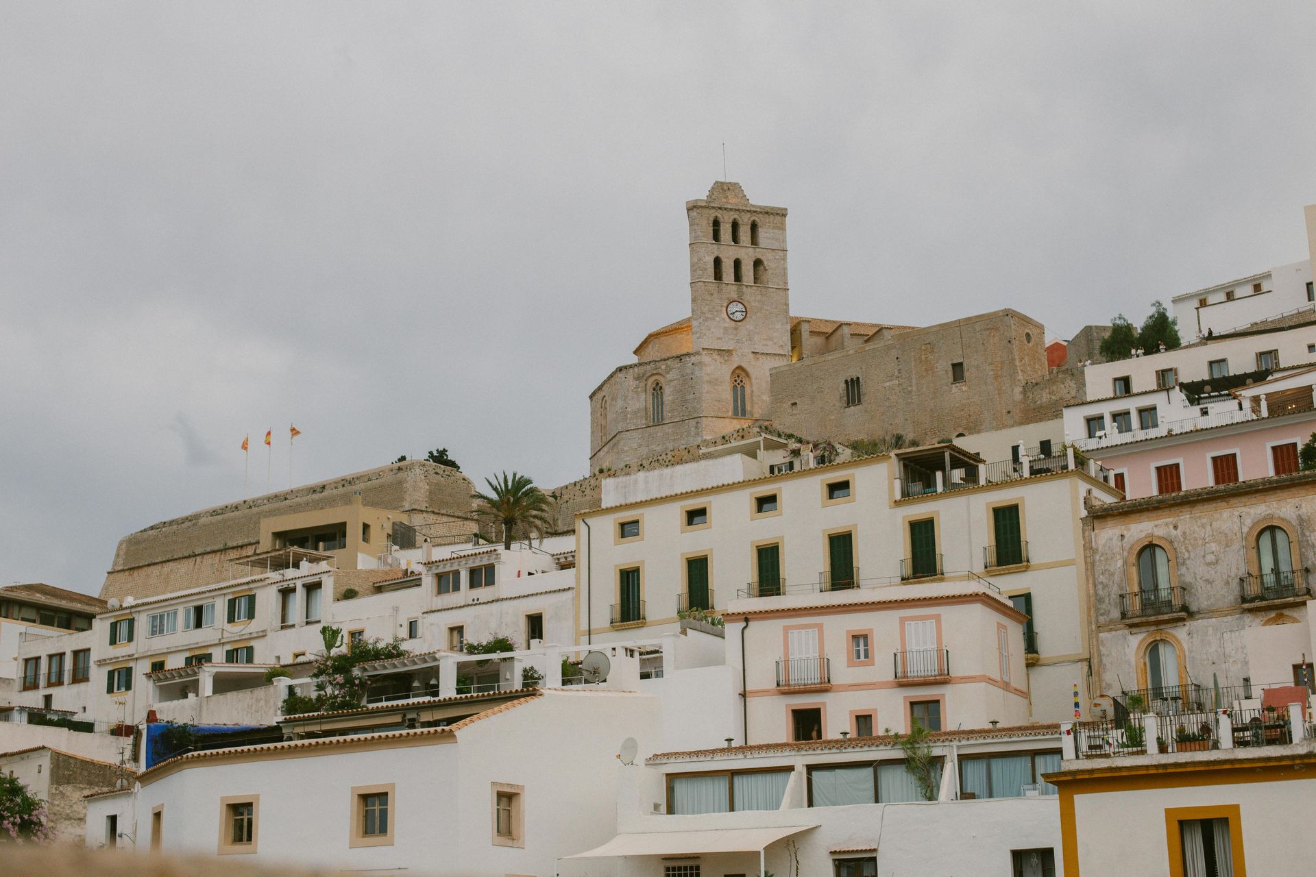 Whitewashed buildings with a church tower on a hillside under an overcast sky.