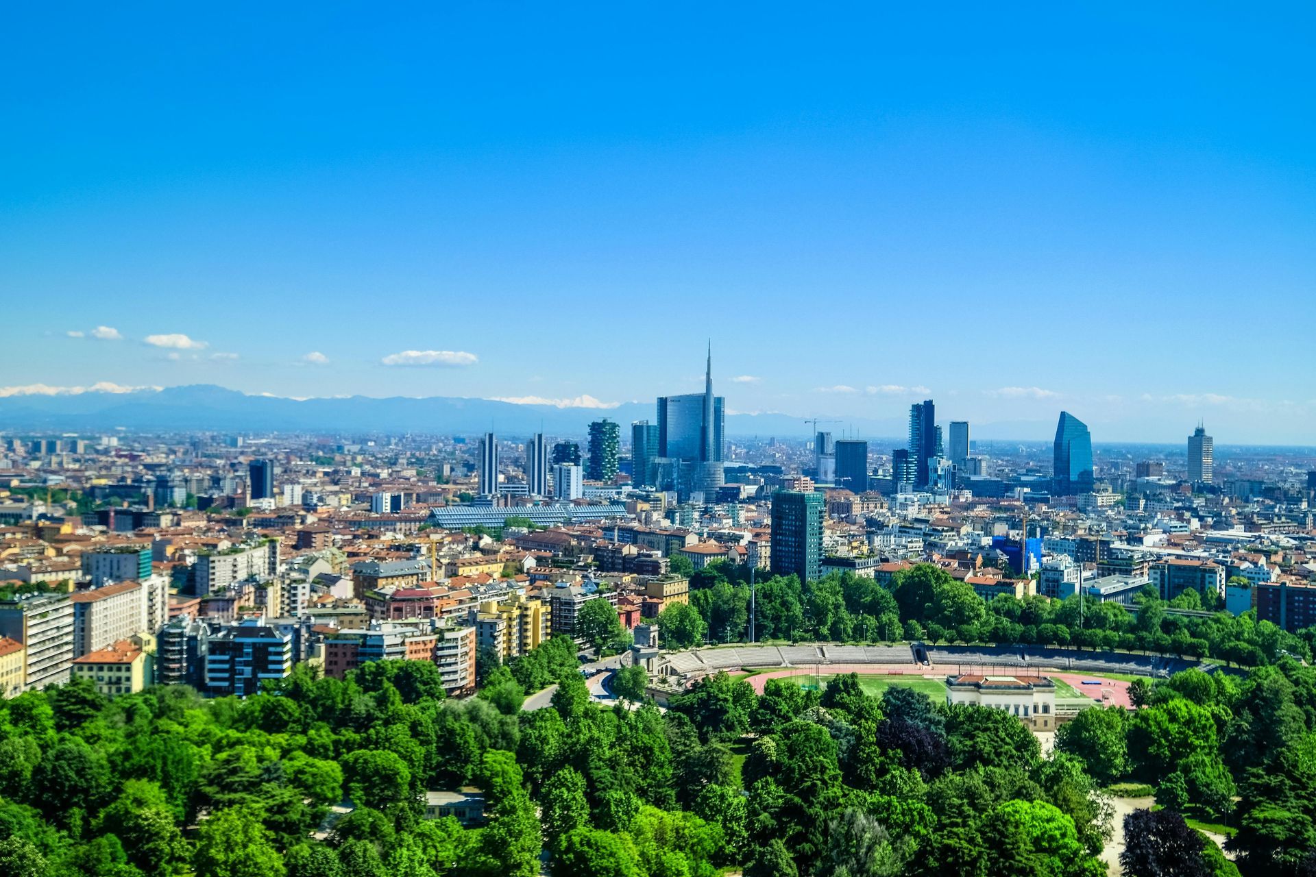Milan skyline with modern skyscrapers, green trees, and blue sky.