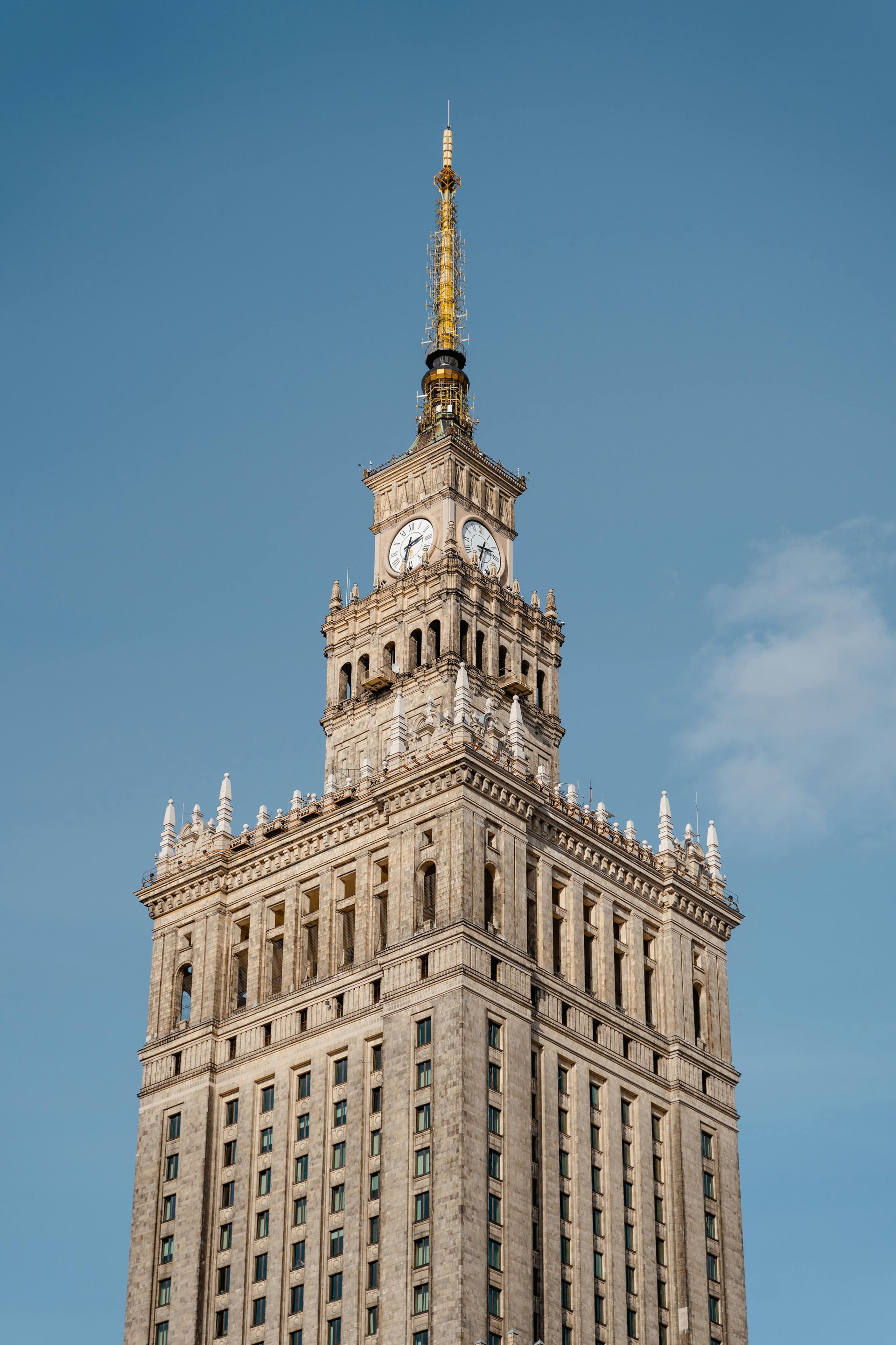 Palace of Culture and Science in Warsaw, Poland; tall gray building with clock tower, blue sky.