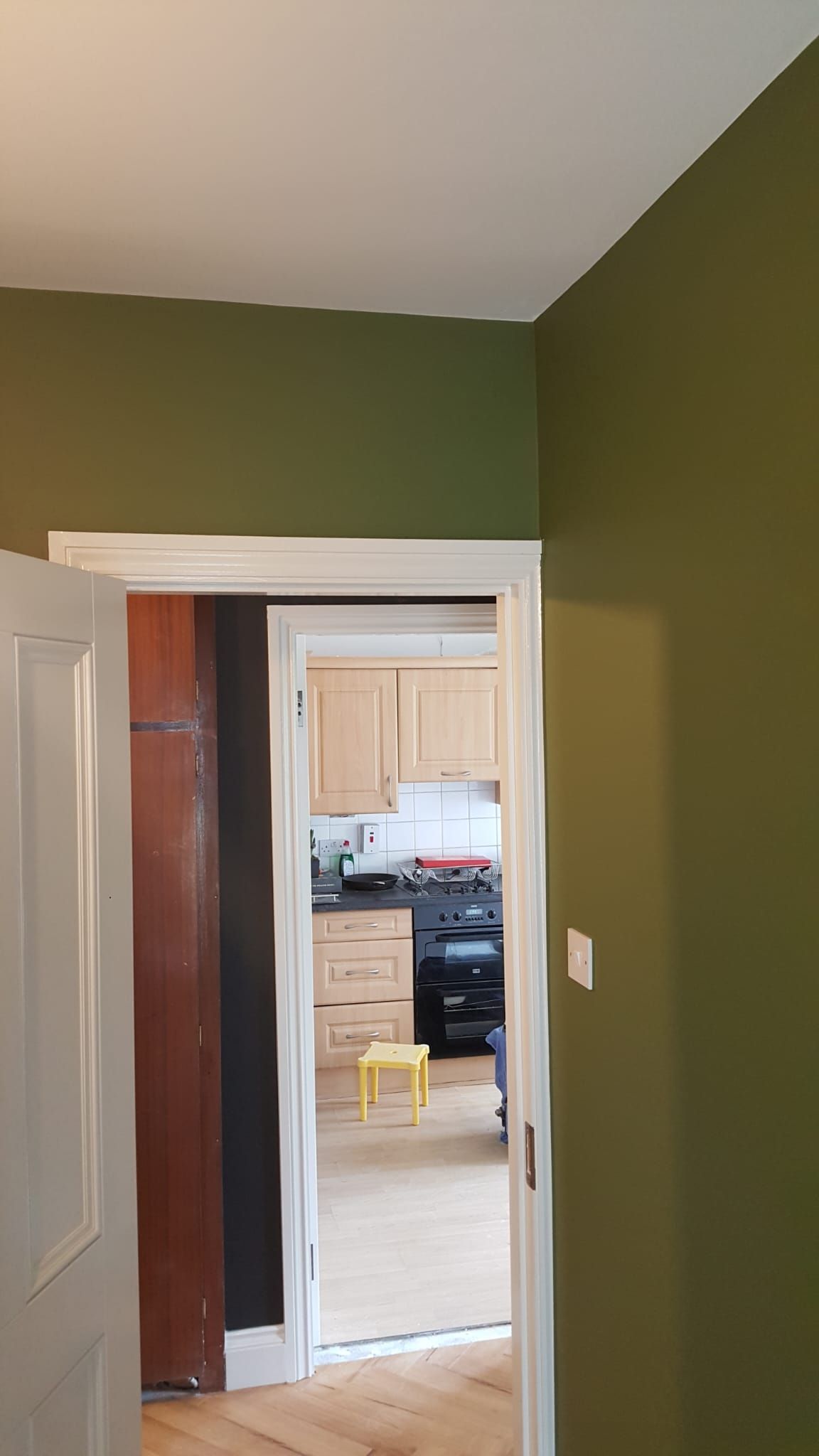 A hallway with green walls and a door leading to a kitchen.