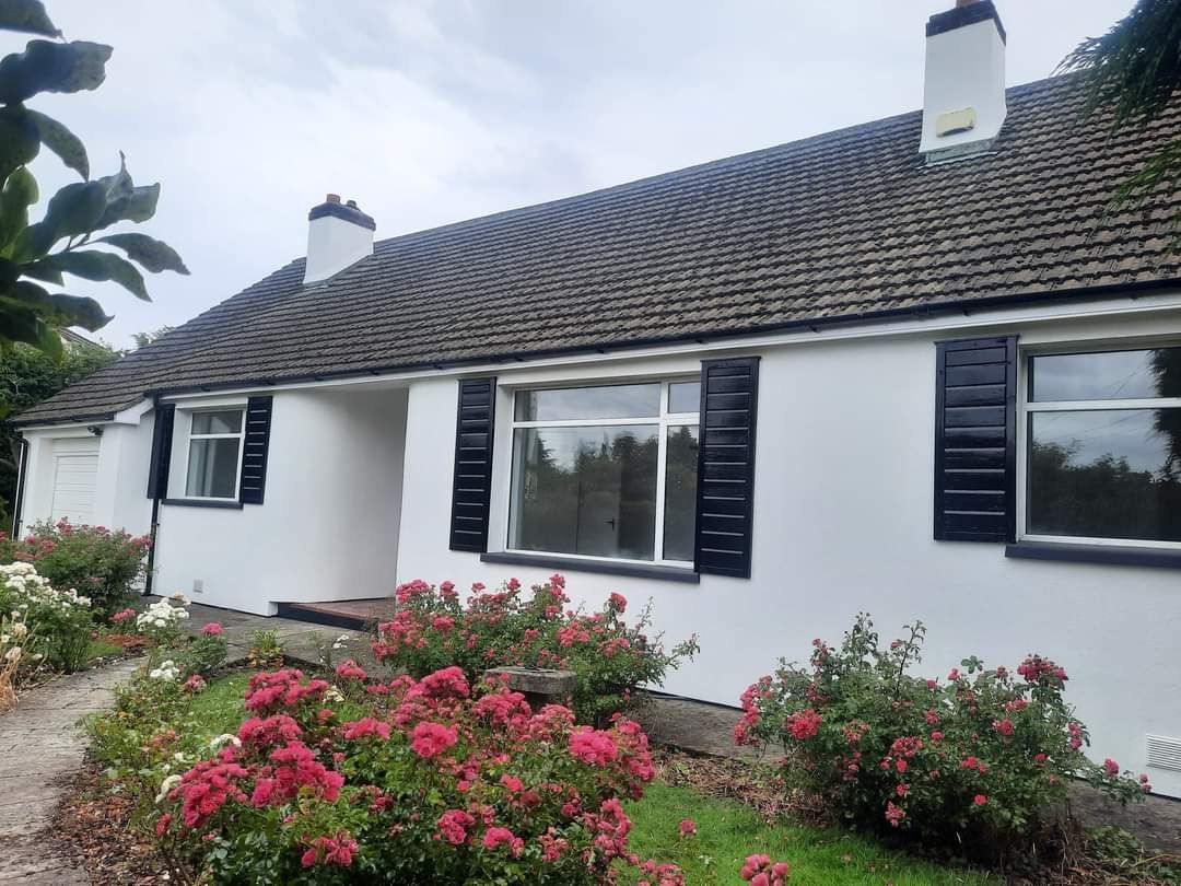 A white house with black shutters and flowers in front of it.