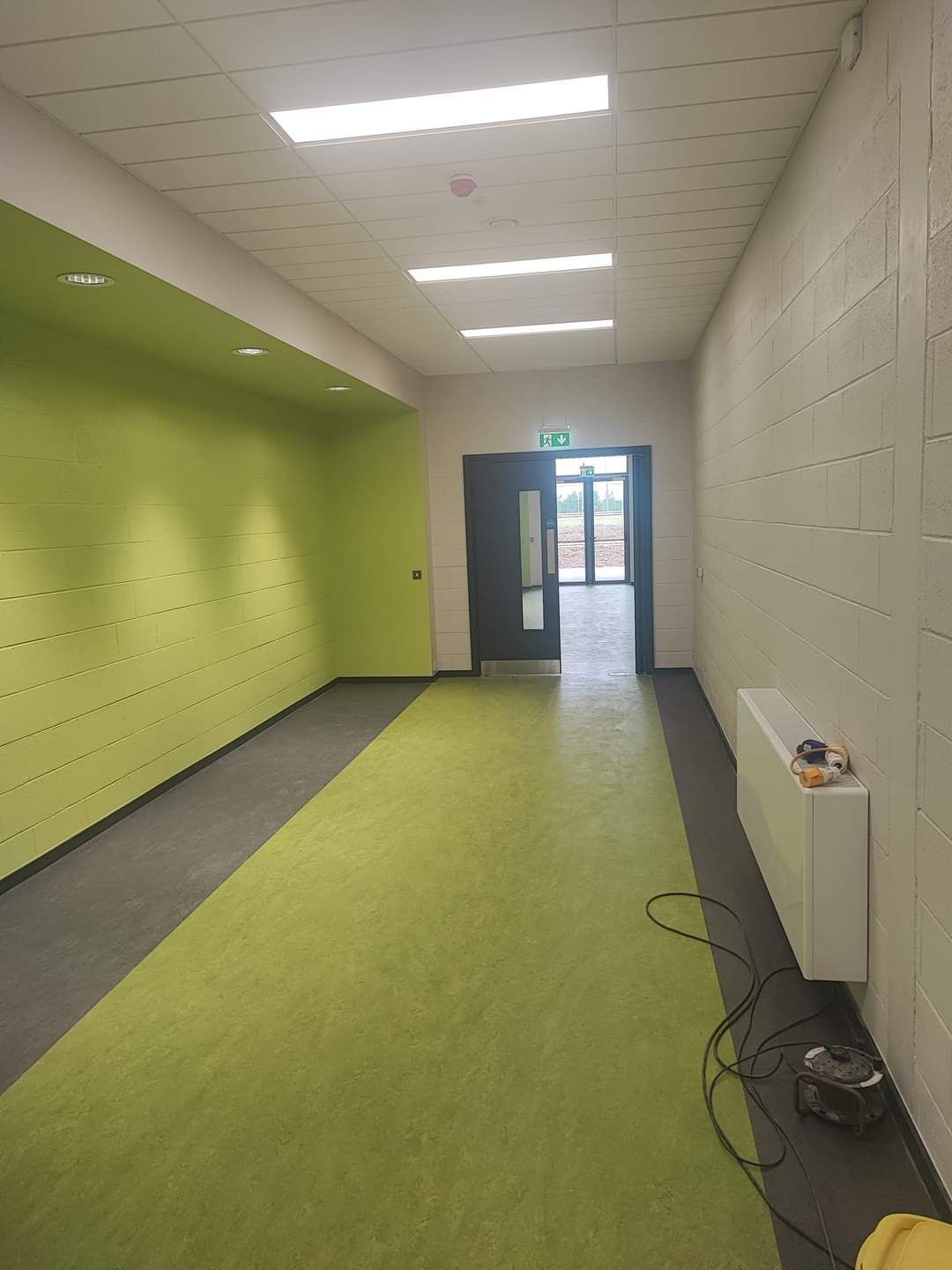 A long hallway with green walls and a green carpet leading to a door.
