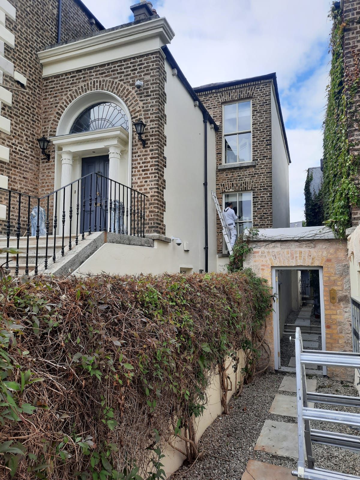 A man is standing on a ladder in front of a large brick building.