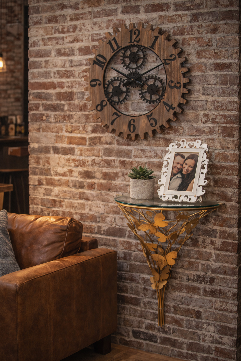 Sopra una consolle semicircolare dorata a forma di farfalla, montata a parete, è appeso un orologio a forma di ingranaggio, sul quale sono appoggiate una foto incorniciata e una pianta.