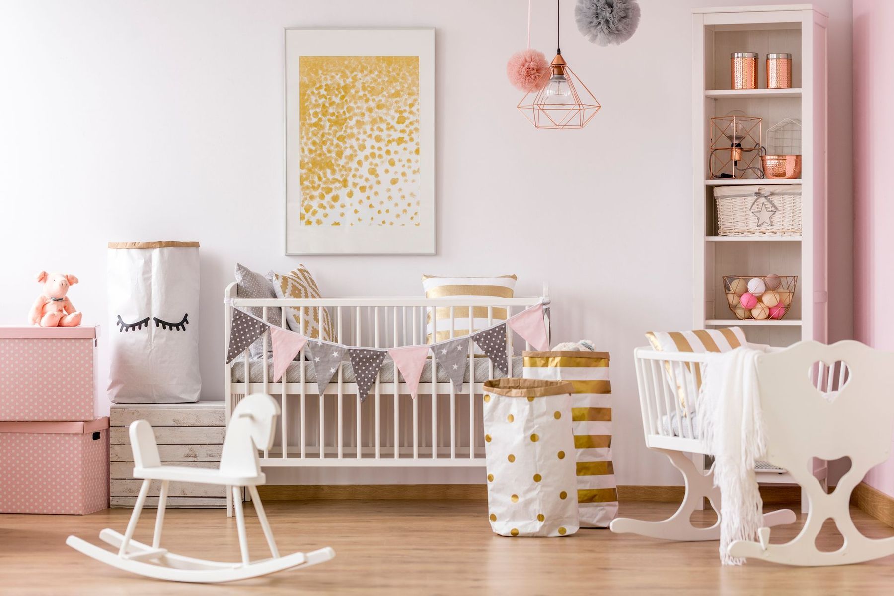 Una cameretta con culla bianca, cavallo a dondolo bianco e libreria, decorata nei toni del rosa, del bianco e dell'oro.