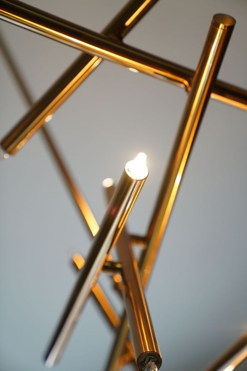 Una moderna lampada a sospensione geometrica color oro con punte illuminate su uno sfondo tenue e chiaro.