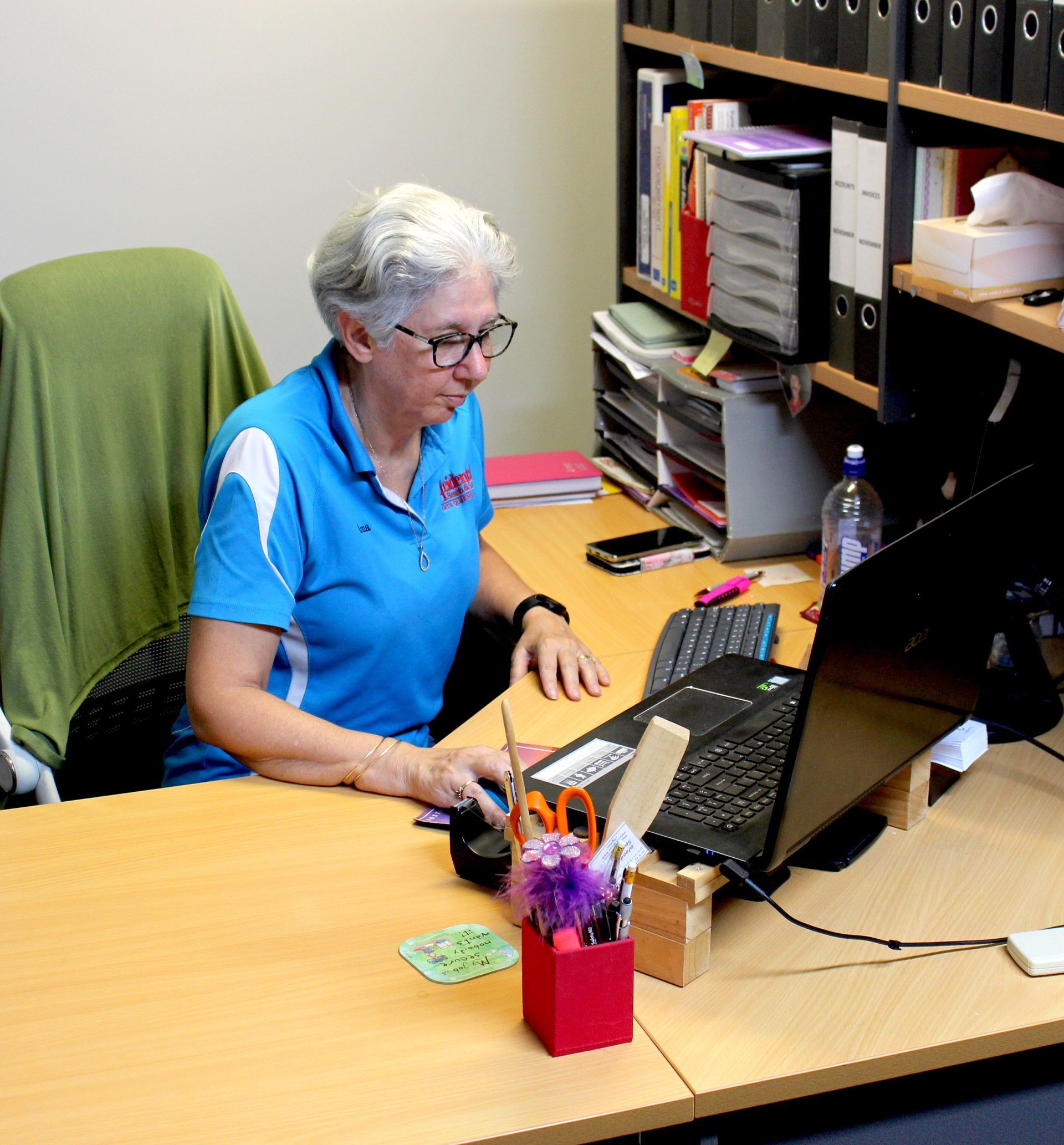 A Woman In A Blue Shirt Sits At A Desk With A Laptop —  Accidental Health & Safety NQ & Mt Isa In Mt Isa, QLD