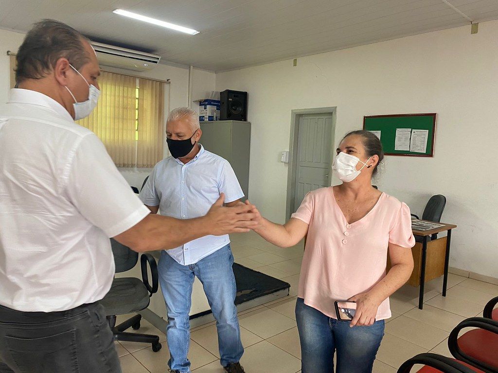 Um homem e uma mulher usando máscaras faciais apertam as mãos em uma sala.