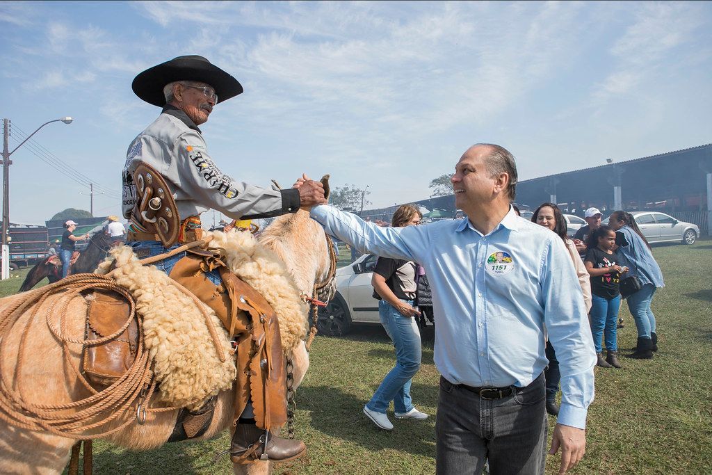 Um homem está de pé ao lado de um homem cavalgando em um campo.
