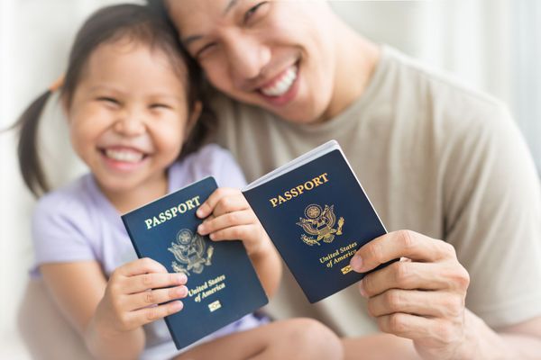A smiling person holding a child, both displaying their United States passports.