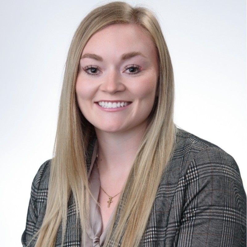 Blonde woman smiling, wearing a gray plaid blazer and gold necklace, against a white background.