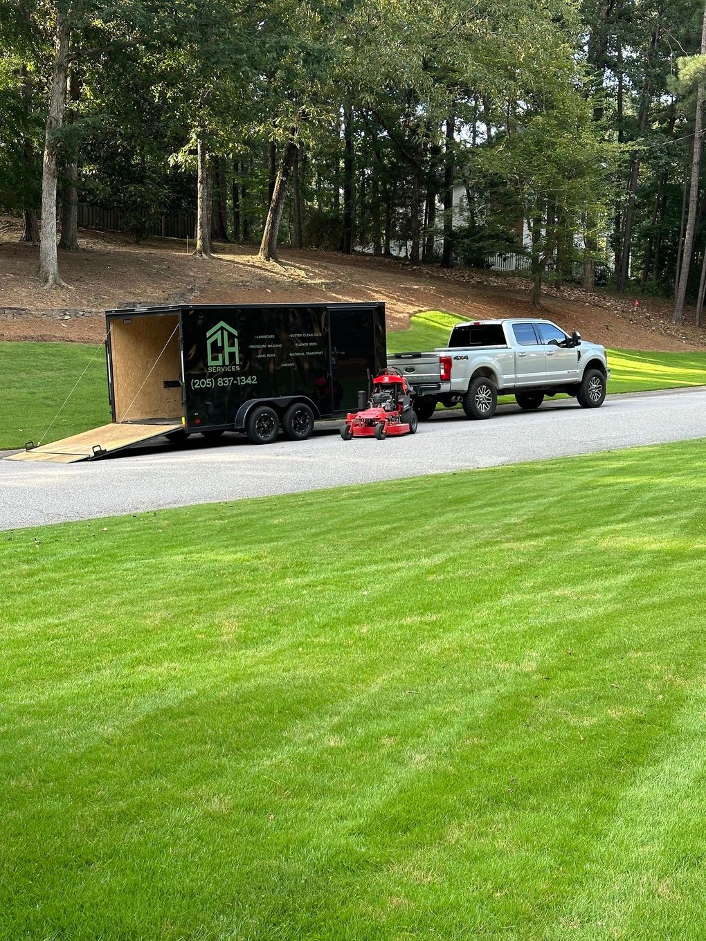 A truck is towing a trailer with a lawn mower in it.