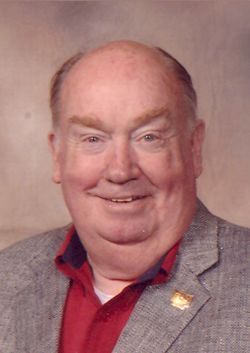 A smiling man with a bald head, wearing a red shirt and gray jacket.