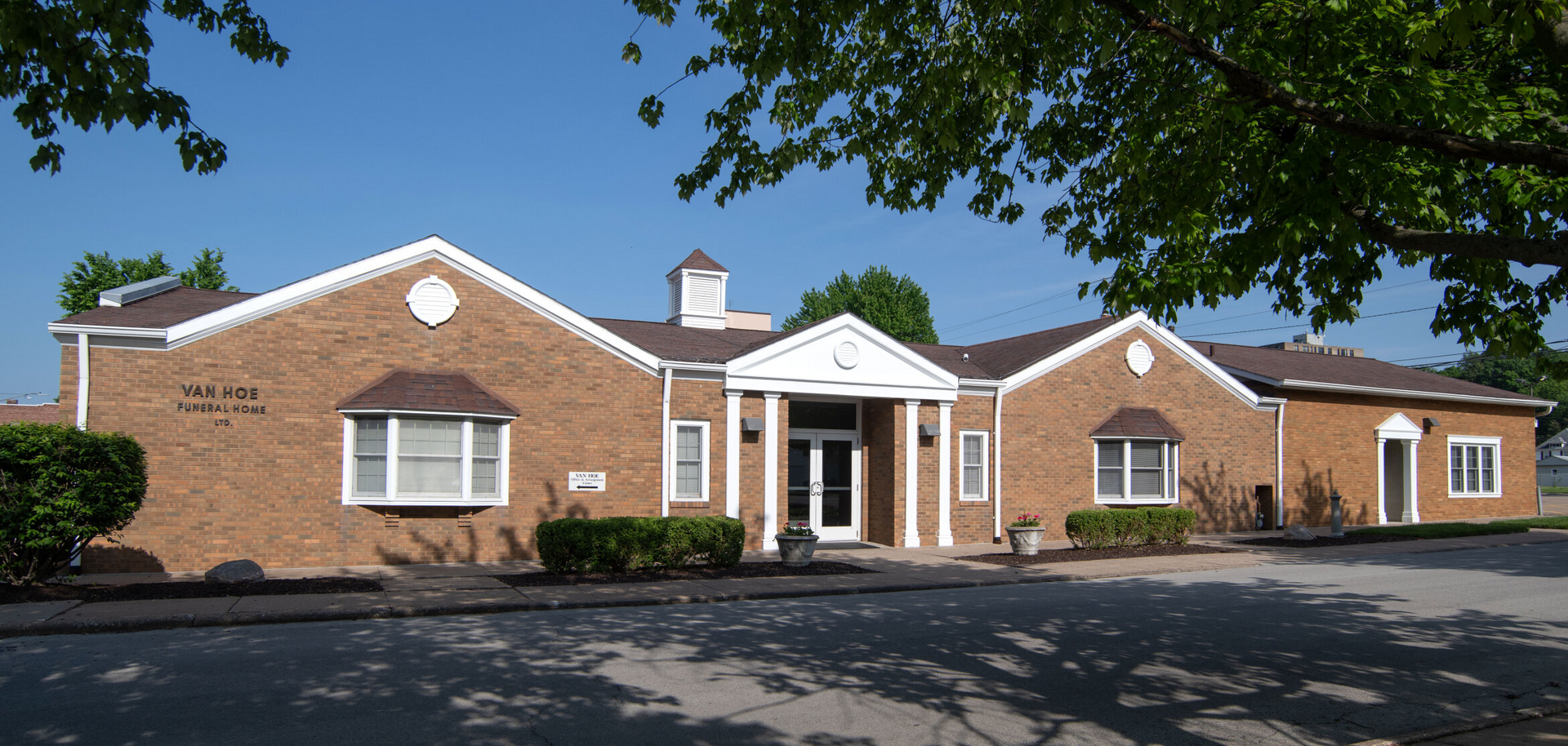 A brick building with white trim, arched windows, and a small cupola under a clear blue sky.