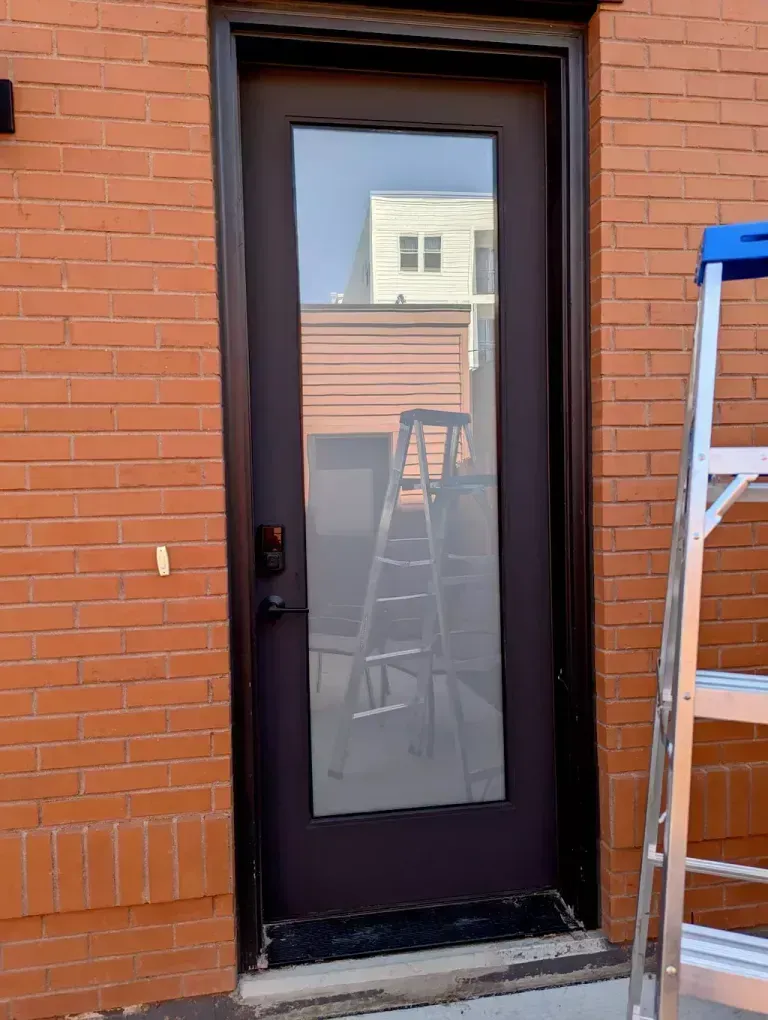 A dark door with a large glass panel set in a red brick wall, a ladder rests nearby.