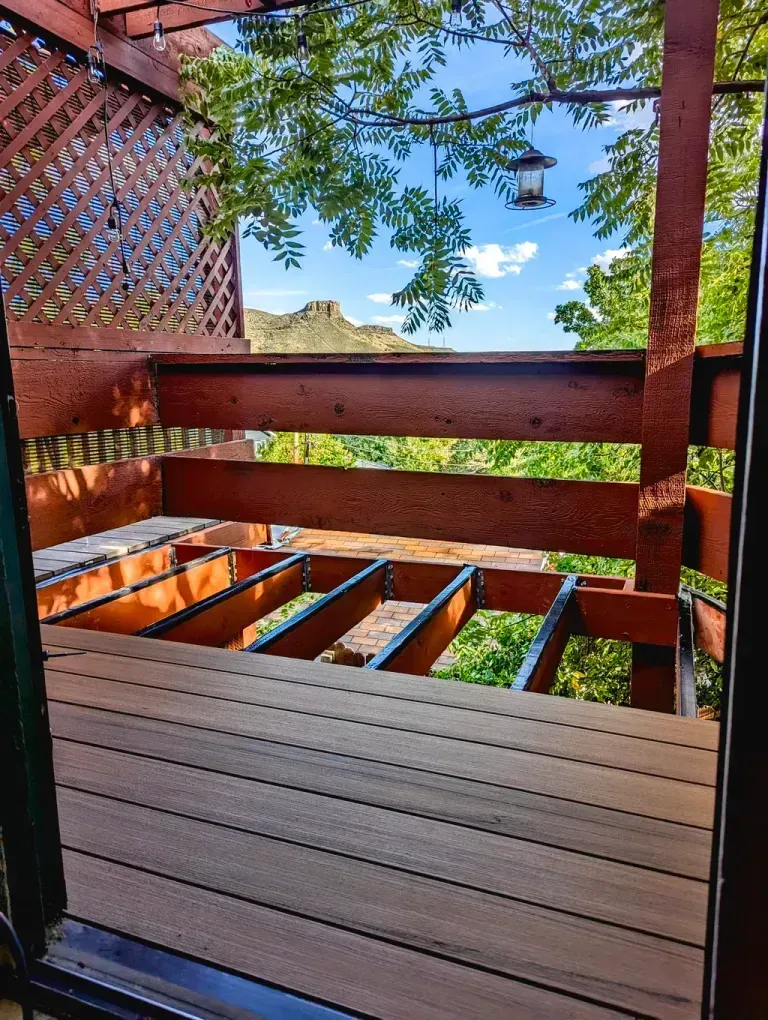Wooden deck overlooking a scenic view of trees, mountains, and blue sky, with lattice fencing and a bird feeder.