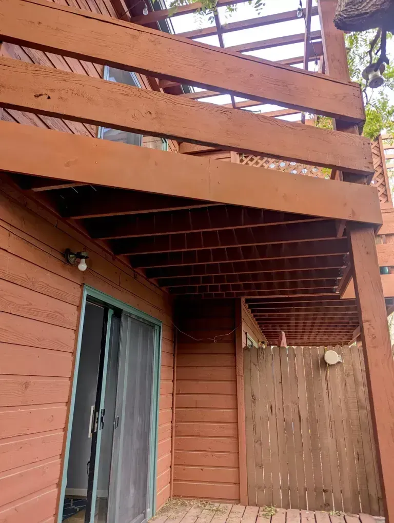 A wooden deck painted brown with a sliding glass door and a wooden fence.
