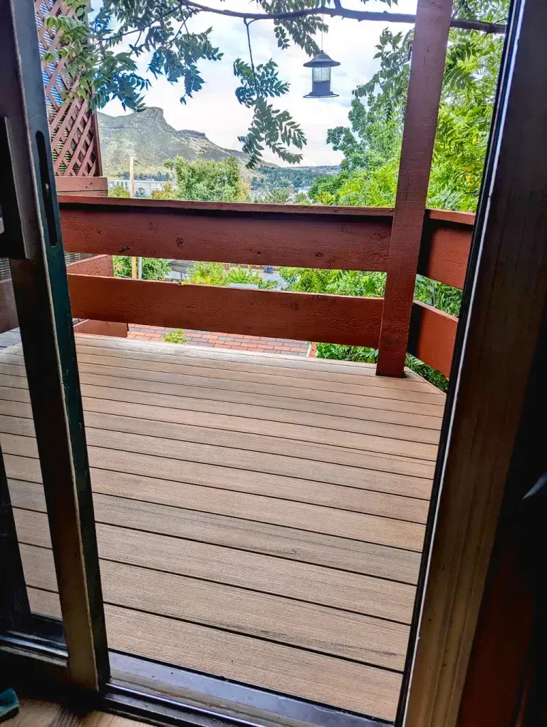 View from a doorway onto a wooden deck with a railing, overlooking a valley with trees and a mountain in the background.