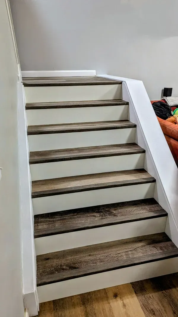 Staircase with wooden treads and white risers. The stairs lead upwards, illuminated by overhead lighting.
