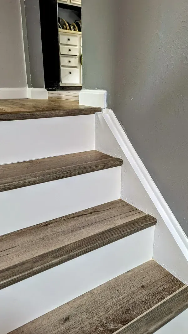 White-painted staircase with wood-look treads, leading upward, a storage unit visible at the top.