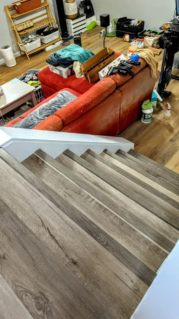 Wooden staircase leads to a cluttered living room with a red sofa.