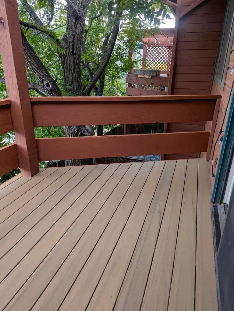 Deck with brown railing and light-colored wooden planks. A tree and foliage are visible in the background.