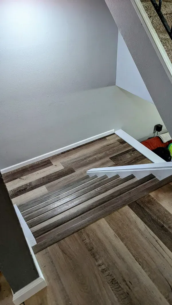 Staircase with wood-look flooring and white trim. The wall is gray, and a corner is visible at the top.