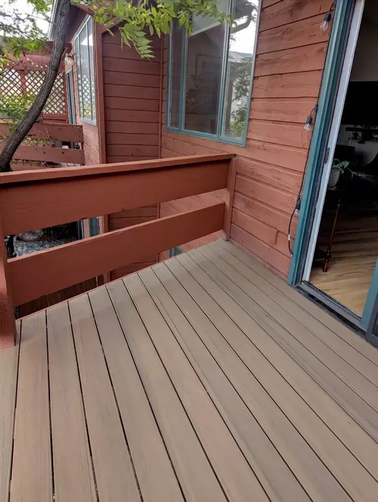 Wooden deck with brown railing and siding. Sliding glass door on right. Light-brown composite decking.