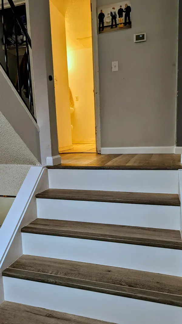 Staircase with white risers, brown treads, and a handrail, leading up to a doorway with bright light inside.