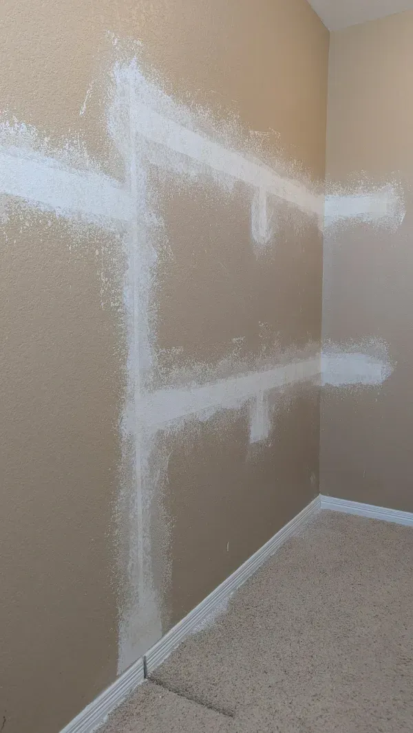 White paint patches on a beige wall, likely covering previous fixtures. The corner of a room with carpet is visible.