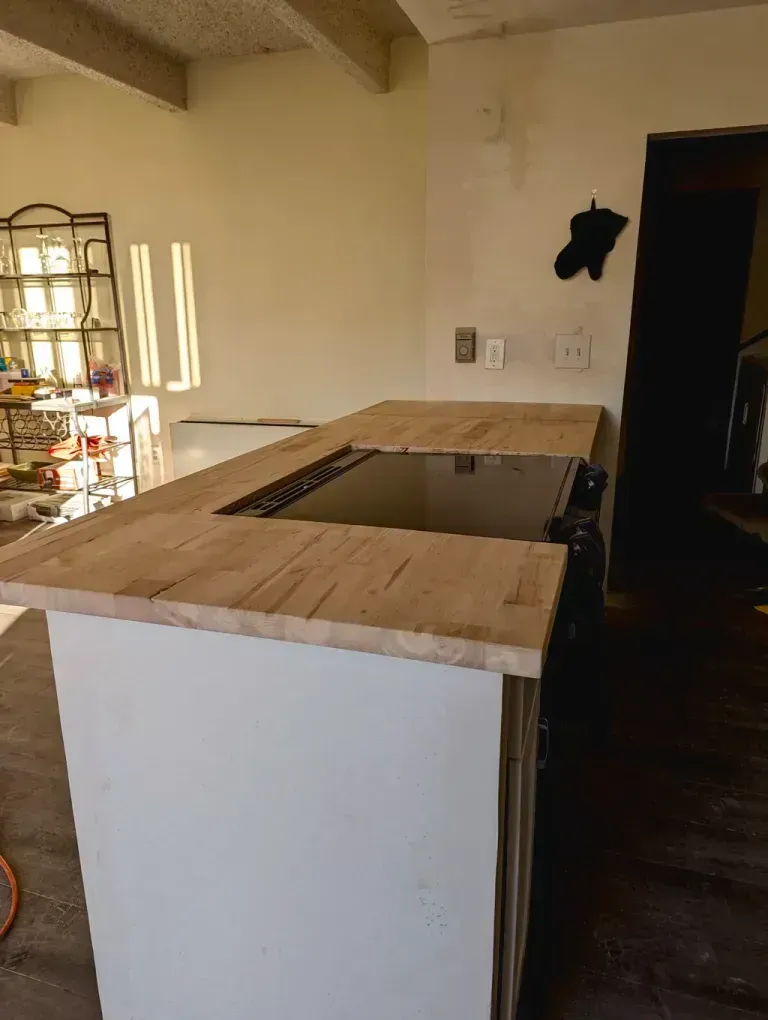 A kitchen island with a wooden countertop. The island has a built-in stovetop and sits in a room with white walls.