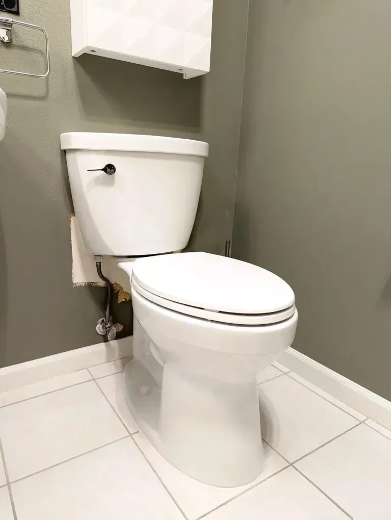 A white toilet in a bathroom with white tile floors and green walls.