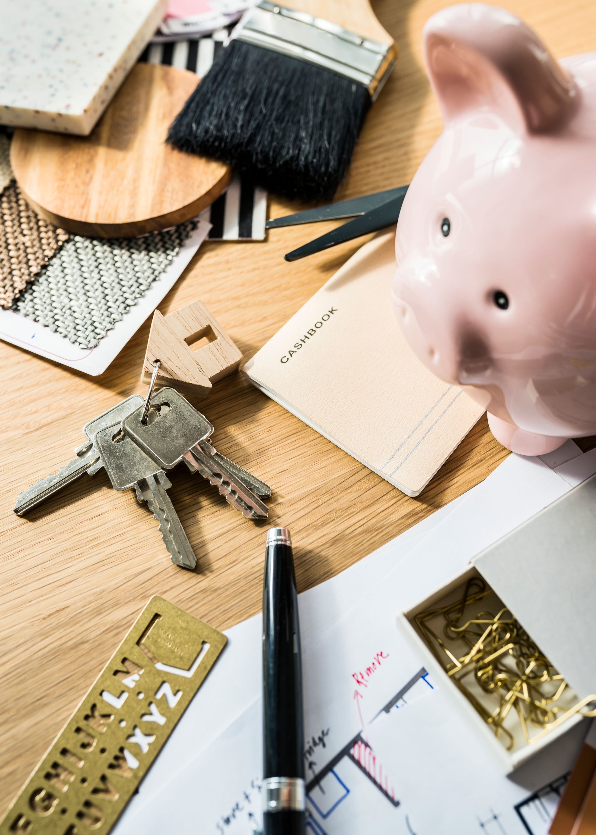 Tirelire, clés et outils de conception sur une table en bois, suggérant une planification de rénovation domiciliaire.
