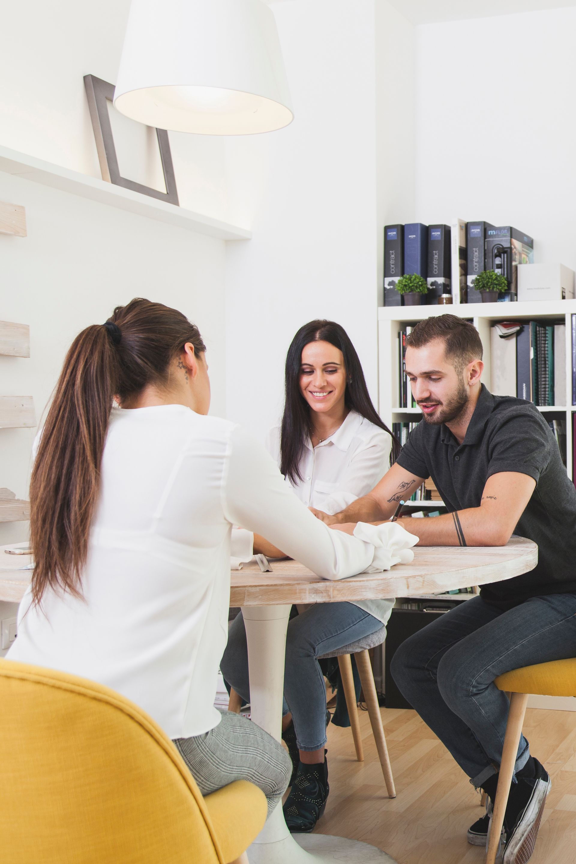 Trois personnes sont assises à une table ronde. Une femme fait des gestes, tandis qu'un couple sourit et écoute.