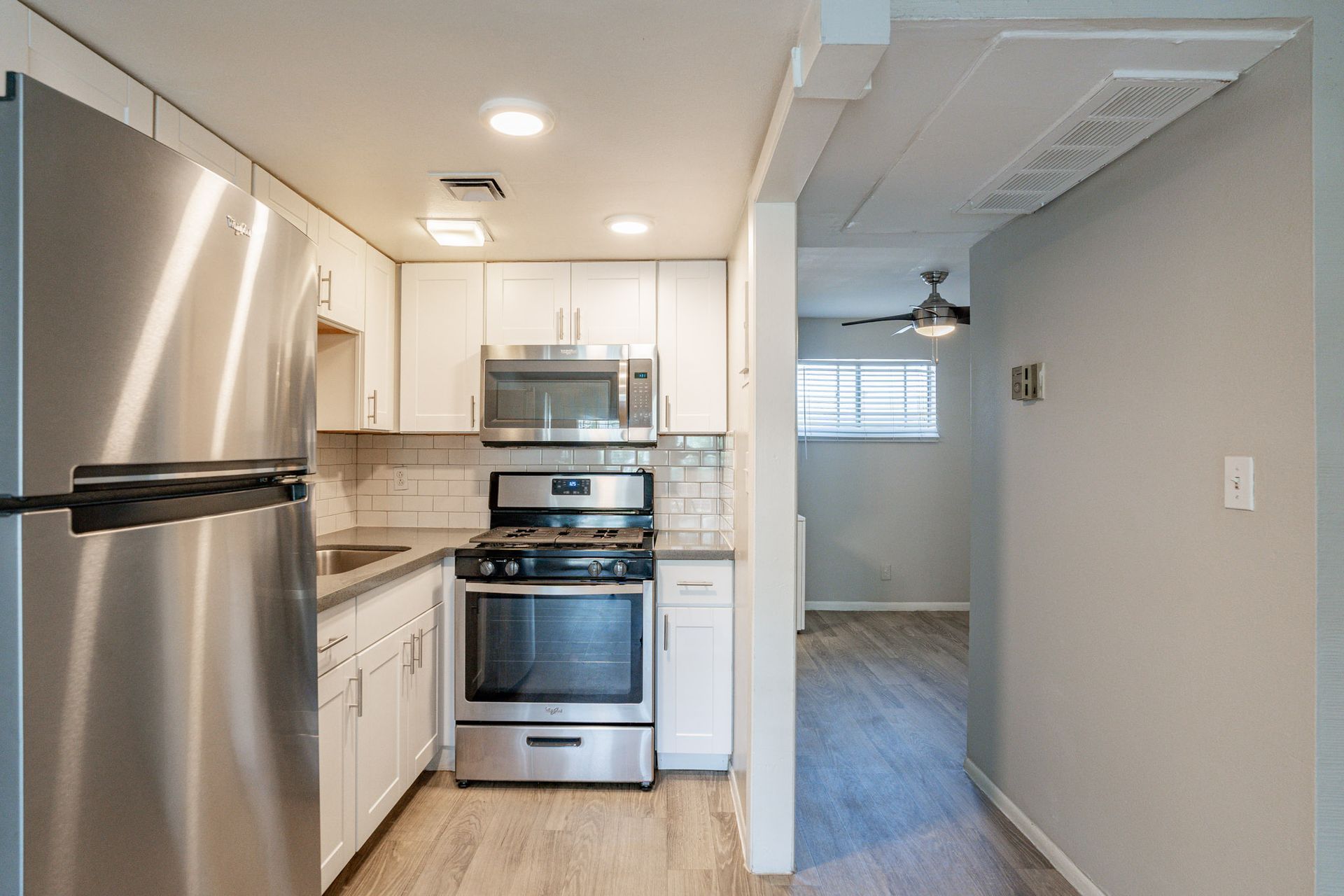 Stainless steel kitchen with white cabinets, appliances, and a hallway to a living space.