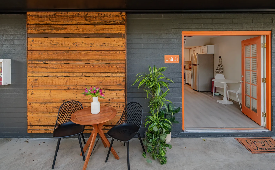 Outdoor seating area with a small table, chairs, plants, and an open doorway.