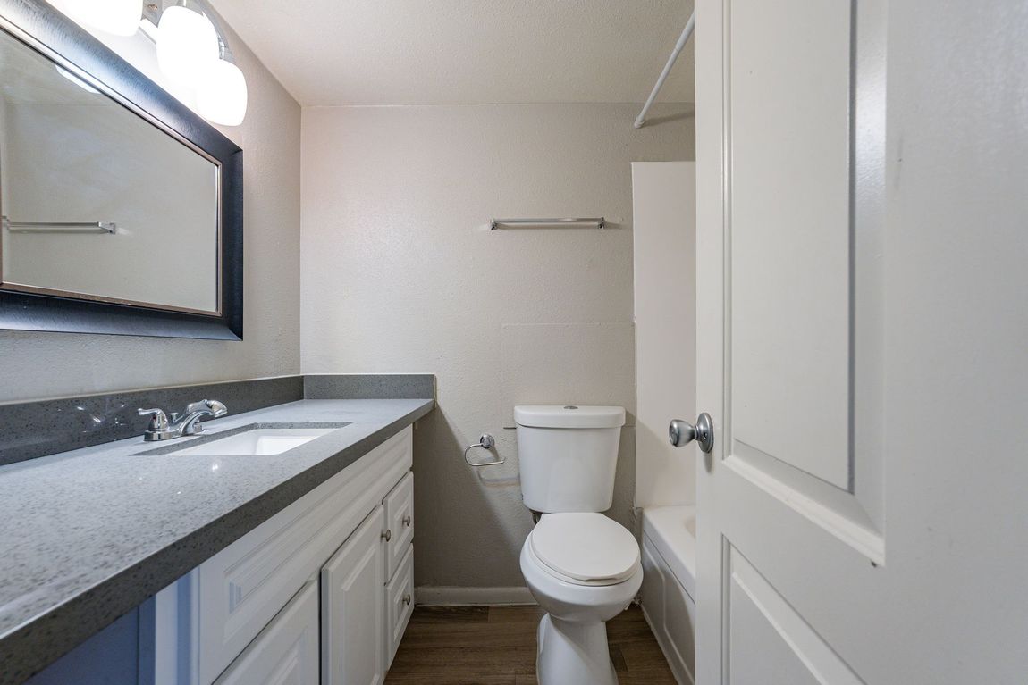 Bathroom with gray countertop, white cabinets, toilet, and a white door.