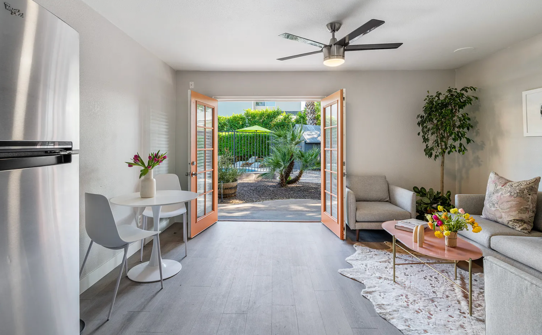Small living space with open doors leading to a garden. Gray walls, light wood floor, and neutral-toned furniture.