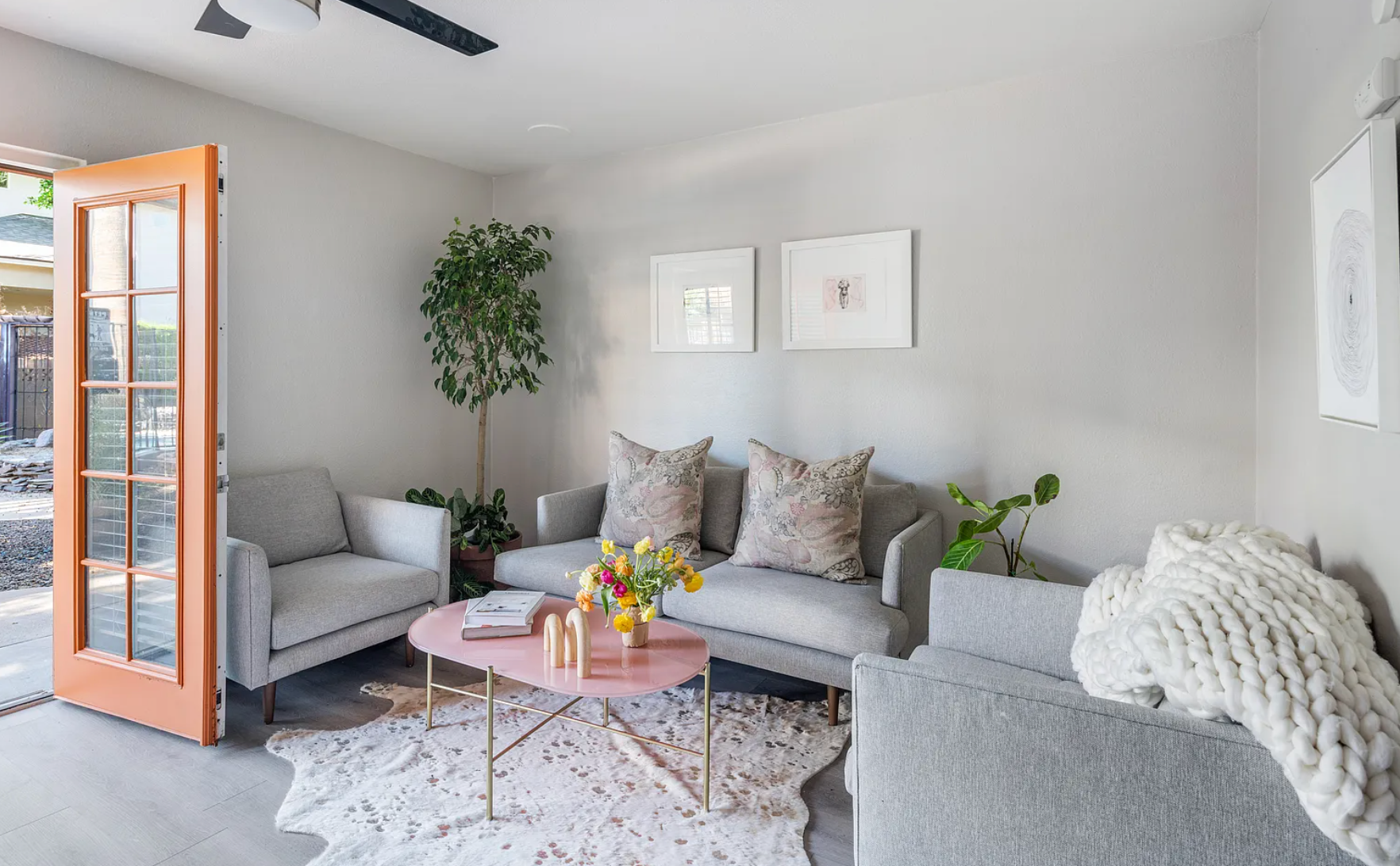 Living room with gray furniture, pink coffee table, open orange door, and art on the wall.